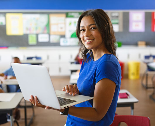 Teacher Holding a Laptop in a Classroom
