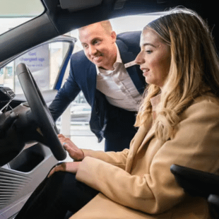 A salesperson talking to a customer in a vehicle.