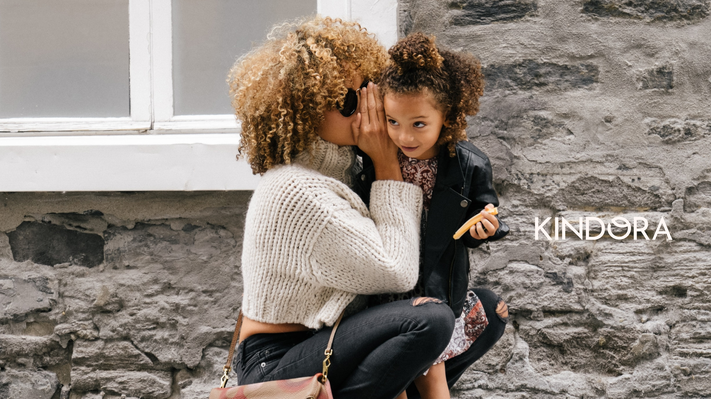 Mum whispering to daughter with Kindora logo